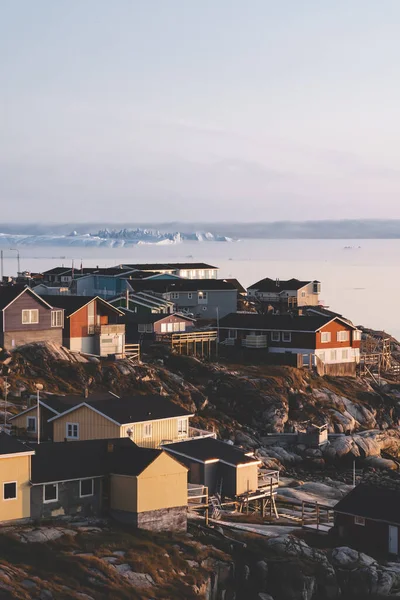 Αεροφωτογραφία της πόλης Ilulissat της Αρκτικής, Γροιλανδία κατά τη διάρκεια της ανατολής του ηλίου με ομίχλη. Πολύχρωμα σπίτια στο κέντρο της πόλης με παγόβουνα στο παρασκήνιο το καλοκαίρι σε μια ηλιόλουστη μέρα με πορτοκαλί ροζ — Φωτογραφία Αρχείου