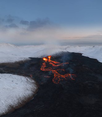Aktif lav nehrinin hava panoraması İzlanda 'nın güneybatısındaki Fagradalsjall Geldingadalir Vadisi' ndeki volkanik bir patlamadan kaynaklanır. Kar dağları olan mavi gökyüzü. Patlama Mart ayı itibariyle devam ediyor.