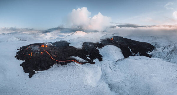 Aerial Panorama of active lava river flows from a volcanic eruption in mount Fagradalsfjall Geldingadalir valley, Southwest Iceland. Blue sky with snow mountains. The eruption is ongoing as of March