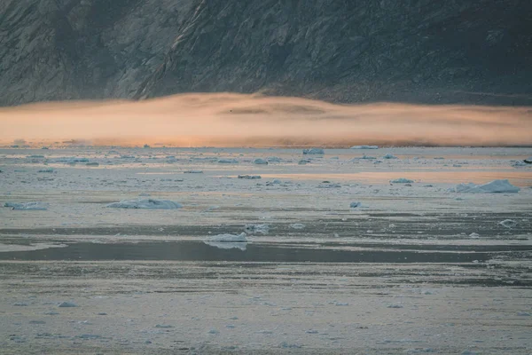 Icebergs varados en la niebla en la boca del fiordo helado cerca de Ilulissat. Naturaleza y paisajes de Groenlandia. Viaje en el barco entre los hielos. Fenómeno del calentamiento global. Costa en la puesta del sol. — Foto de Stock