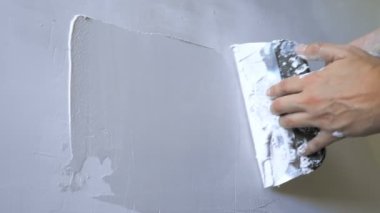 Bir ele yakın çekim. Bir adam duvara bir malayla sıva uygular.