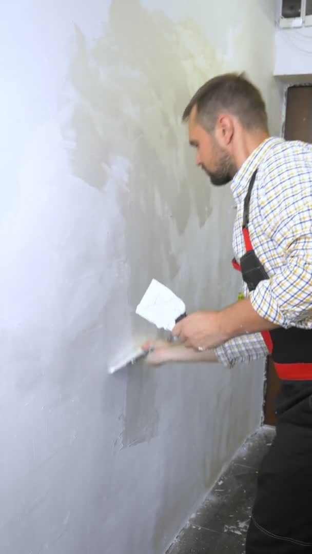 Vertical. joven hombre guapo trabajador de la construcción pone yeso en la pared con una paleta — Vídeos de Stock