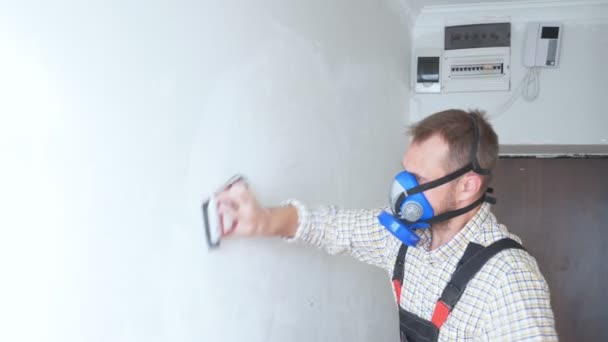 En arbetare i respirator slipar väggen med sandpapper. — Stockvideo