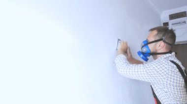 Solunum cihazındaki bir işçi zımpara kağıdıyla duvarı öğütüyor.