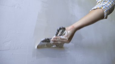 Bir ele yakın çekim. Bir adam duvara bir malayla sıva uygular.