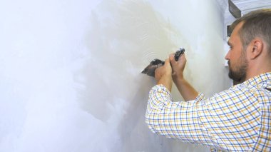 Genç yakışıklı müteahhit duvara bir malayla sıva yapıyor. ev onarımı