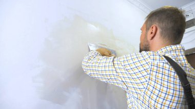 Genç yakışıklı müteahhit duvara bir malayla sıva yapıyor. ev onarımı