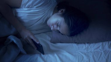 Genç kız gece yatakta yatarken akıllı telefon kullanıyor..
