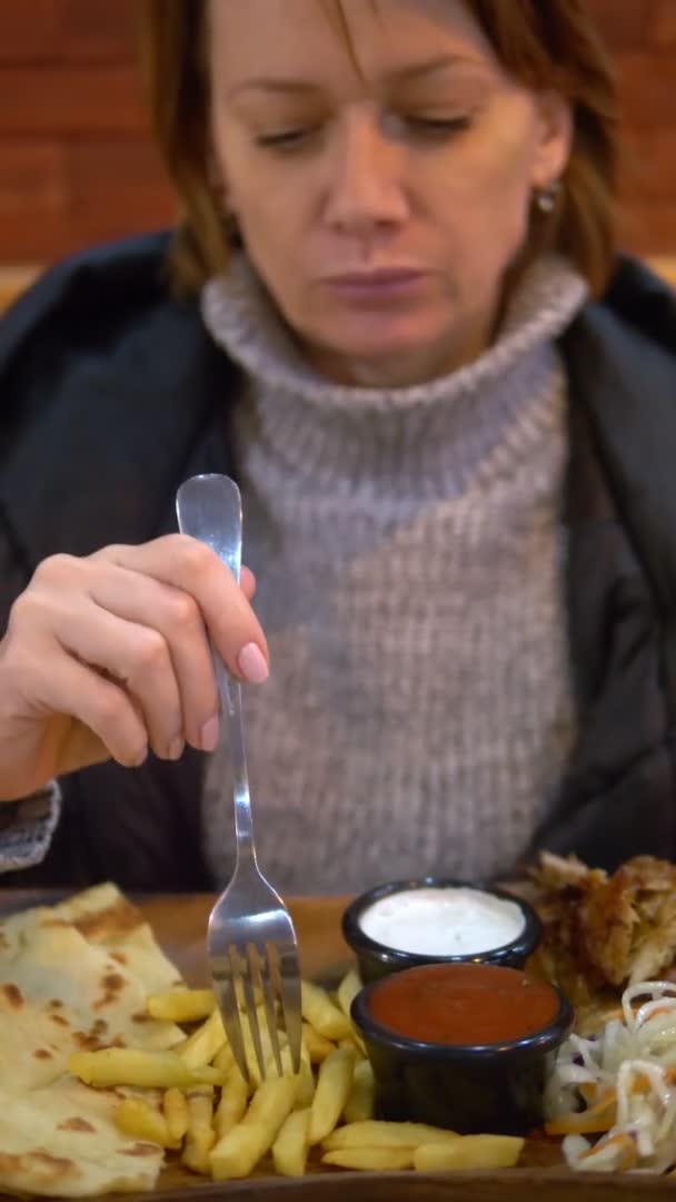 Pionowe. kobieta w swetrze i kurtce jedząca żyroskopy z frytkami w kawiarni fast food — Wideo stockowe