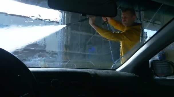 Vista desde el interior del coche. un hombre lavando un coche en un lavadero de coches — Vídeo de stock