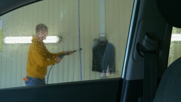 Vista desde el interior del coche. un hombre lavando un coche en un lavadero de coches — Vídeo de stock