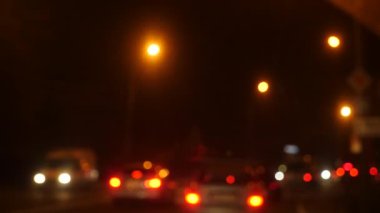 Gece araba sürüyorum. Şehirdeki bulanık arabalar. Şehrin caddelerinde bulanık trafiği olan aydınlatılmış ön araba penceresi. 4k
