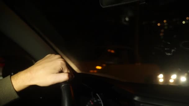 Main sur le volant de la voiture. Bonsoir, la nuit. Circulation à gauche. 4k. au ralenti, lumières floues devant la fenêtre. — Video