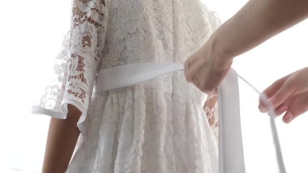 Quelqu'un attache une ceinture sur une robe en dentelle blanche d'une petite fille. 4k, tir au ralenti, éblouissement de la lumière du soleil — Video