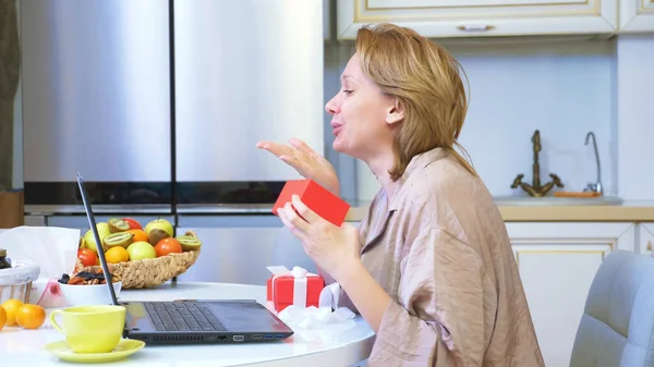 Mujer abre una caja con un regalo mientras está sentado en casa delante de un ordenador portátil. — Foto de Stock