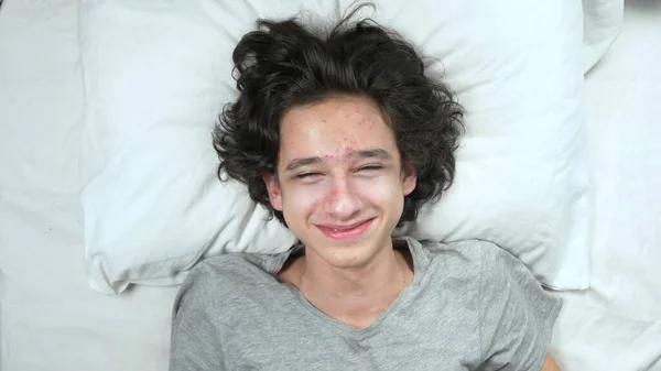 Vy ovanifrån. Porträtt av en stilig ung skrattande kille liggande på sängen — Stockfoto