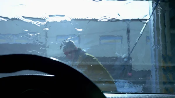 view from inside the car. a man washing a car at a car wash