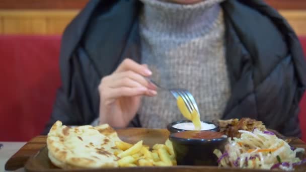 Kobieta w swetrze i kurtce jedząca żyroskopy z frytkami w kawiarni fast food — Wideo stockowe