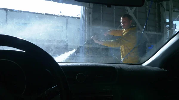 view from inside the car. a man washing a car at a car wash