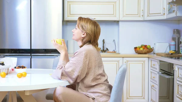 Sonriendo, soñando mujer bebiendo té en casa en su cocina — Foto de Stock