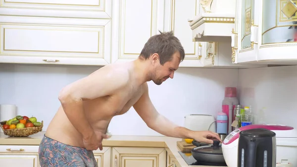 Głodny goły klatka piersiowa człowiek sprawdza patelnię na kuchence — Zdjęcie stockowe