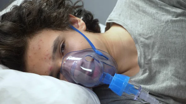 Oxigénmaszk egy fickó arcán, aki az ágyon fekszik egy kórházban. — Stock Fotó