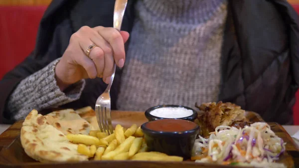 Donna in maglione e giacca mangiare giroscopi con patatine fritte in un bar fast food Foto Stock