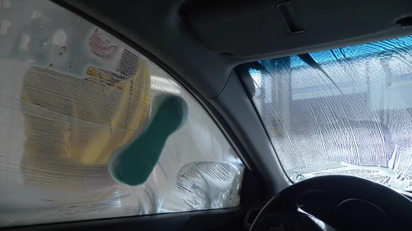 Vista dall'interno della macchina. un uomo che lava un'auto in un autolavaggio Foto Stock