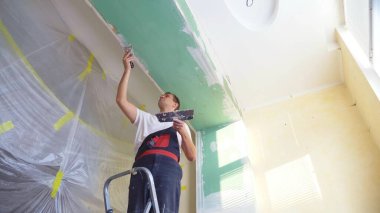 Tulumlu bir adam duvara bir spatula ile sıva uygular.
