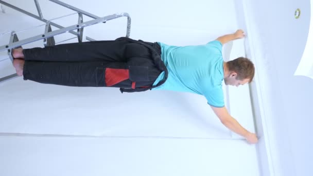 Video vertikal. seorang pria di overall glues wallpaper di dinding di apartemen — Stok Video