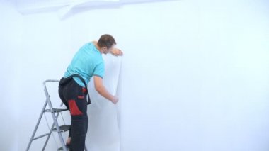 Tulumlu bir adam bir apartmanın duvarlarına duvar kağıdı yapıştırıyor.