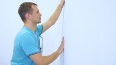 Tulumlu bir adam bir apartmanın duvarlarına duvar kağıdı yapıştırıyor.