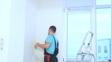 Tulumlu bir adam bir apartmanın duvarlarına duvar kağıdı yapıştırıyor.