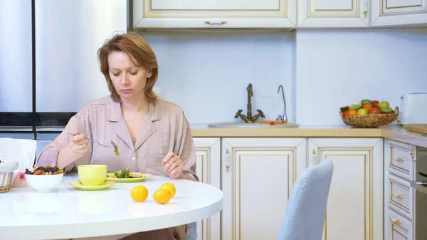 Mujer comiendo mientras está sentada en la cocina en la mesa en casa — Foto de Stock