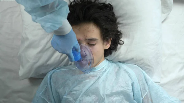 Oxigénmaszk egy fickó arcán, aki az ágyon fekszik egy kórházban. — Stock Fotó