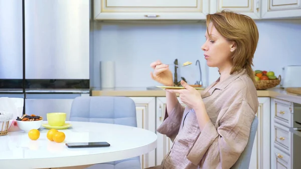 Mujer comiendo mientras está sentada en la cocina en la mesa en casa — Foto de Stock