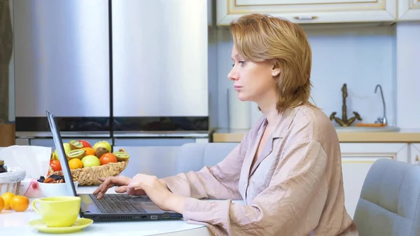 Piękna kobieta pracuje na laptopie siedząc w domu w kuchni — Zdjęcie stockowe