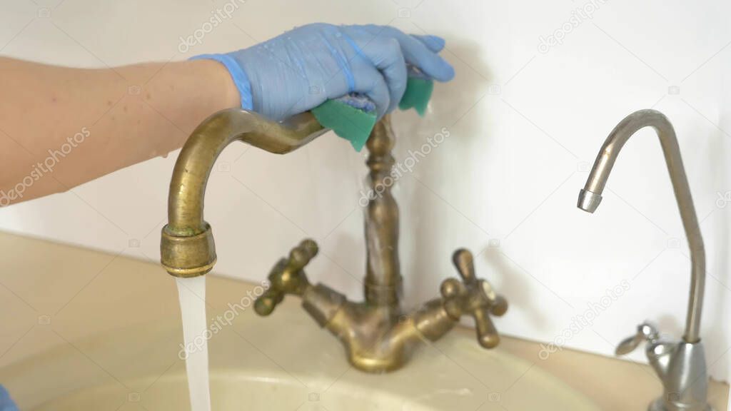  female hands in rubber gloves wash a brass faucet with water in the kitchen 