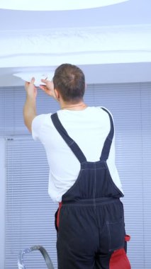 dikey video. Tulumlu genç bir adam duvara duvar kağıdı yapıştırıyor.