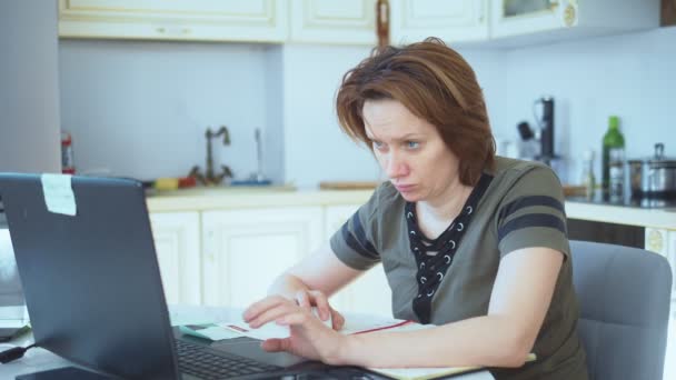 Kobieta pracująca na laptopie z papierowymi dokumentami w domu w kuchni — Wideo stockowe