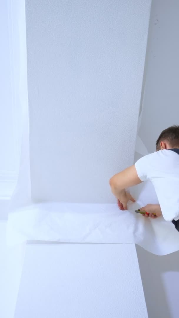 Pionowe wideo. młody mężczyzna w kombinezonie przykleja tapetę do sufitu — Wideo stockowe