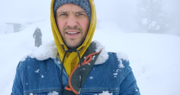 Человек в теплой джинсовой куртке идет по пустынной снежной дороге — стоковое видео
