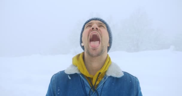 Portrait of a cheerful man who catches snowflakes with his mouth outdoors — Stock Video