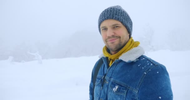 Portrét pohledného muže v parku během sněžení. usměje se a podívá se do kamery — Stock video