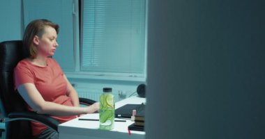 İş yerinde dizüstü bilgisayarda çalışan ve limon ve salatalıkla detoks suyu içen bir kadın.