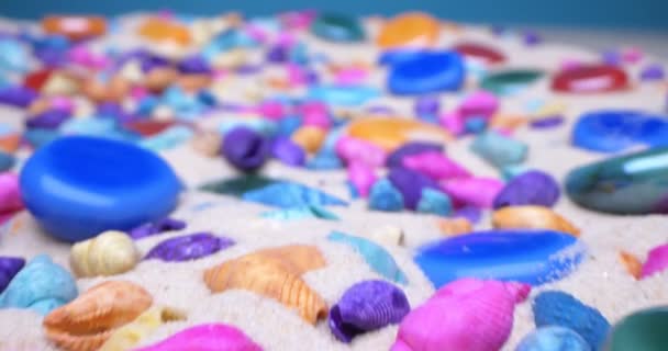 Detaillierte extreme Nahaufnahme von bunten Muscheln und polierten Glassteinen auf weißem Sand — Stockvideo
