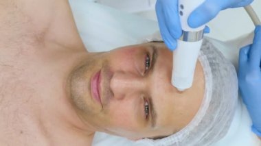 Güzellik uzmanının resepsiyonunda bir adamın yüzüne yakın çekim. Sıkıştırılmış hava ile enjeksiyon olmayan kozmetoloji. İğne olmayan enjeksiyonların tanıtımı 
