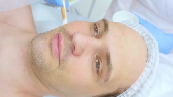 Косметолог наносит маску с кистью на лицо человека. макро — стоковое видео
