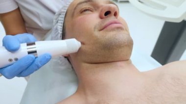 Güzellik uzmanının resepsiyonunda bir adamın yüzüne yakın çekim. Sıkıştırılmış hava ile enjeksiyon olmayan kozmetoloji. İğne olmayan enjeksiyonların tanıtımı 