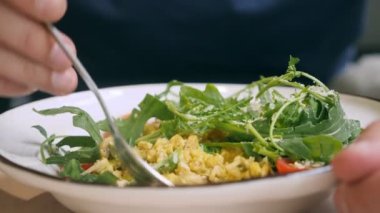 Yakın plan, birisi mantarlı ve mikro yeşillikli vegan arpa tabağıyla yemek yiyor.